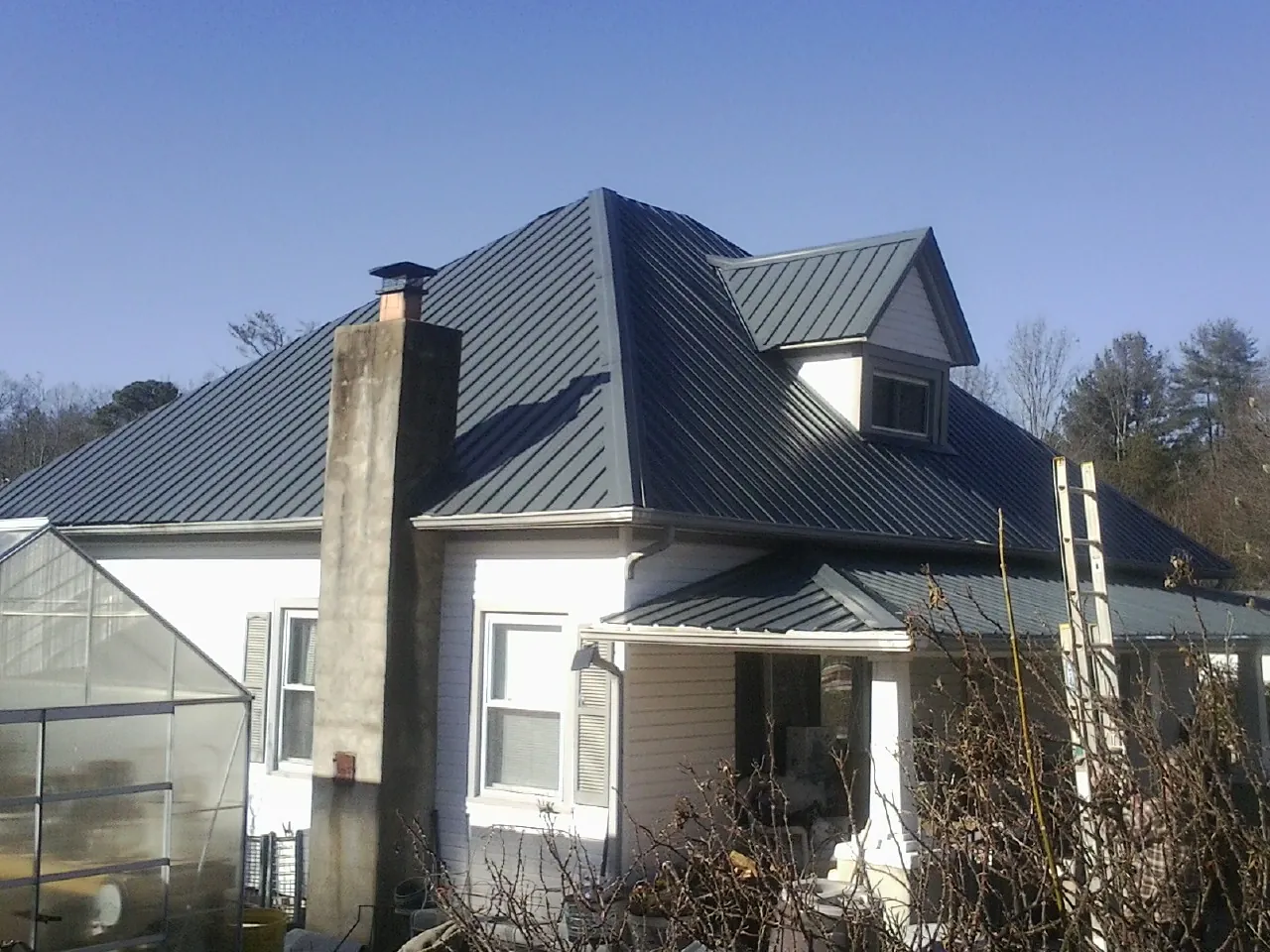 Dark blue standing seam metal roof on a white farmhouse with dormer — Slate & Tile Roof Repair by Roofing Brothers in Furman