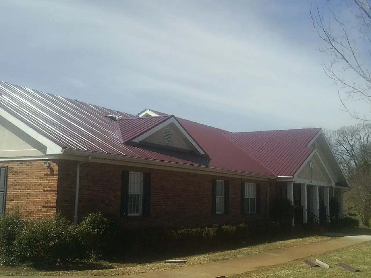 Red metal roof with gabled entries on a long brick building, from a Hail Damage Roof Repair job in Furman