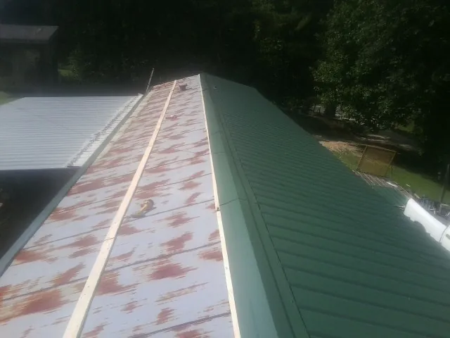 Old rusted panels beside newly installed green metal roofing — Wind Damage Roof Repair by Roofing Brothers in Furman