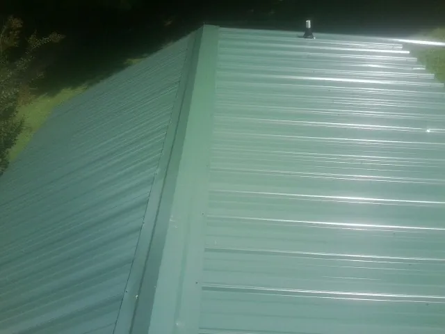 New green metal panels meeting at the ridge of a roof — Flat Roof Repair work by our crew in Furman