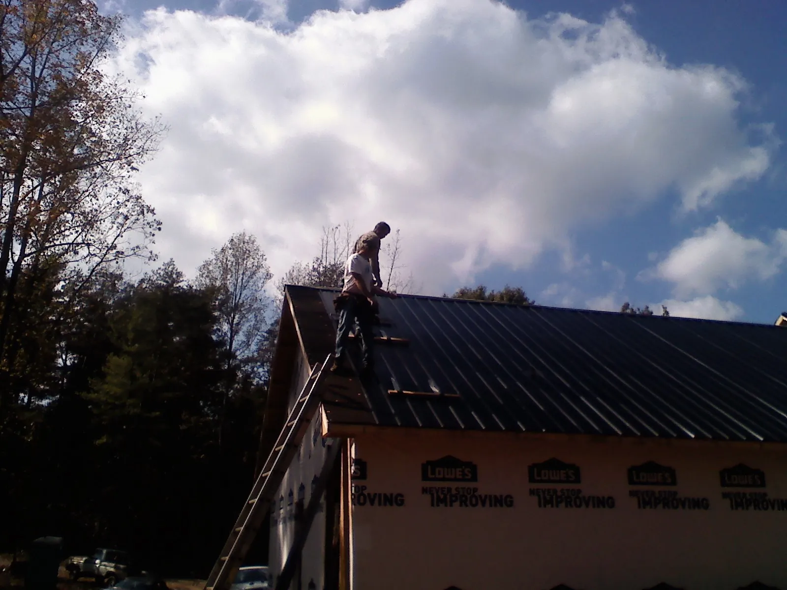 Roofer fastening dark metal panels high against a cloudy sky, from a Roof Inspection job in Furman