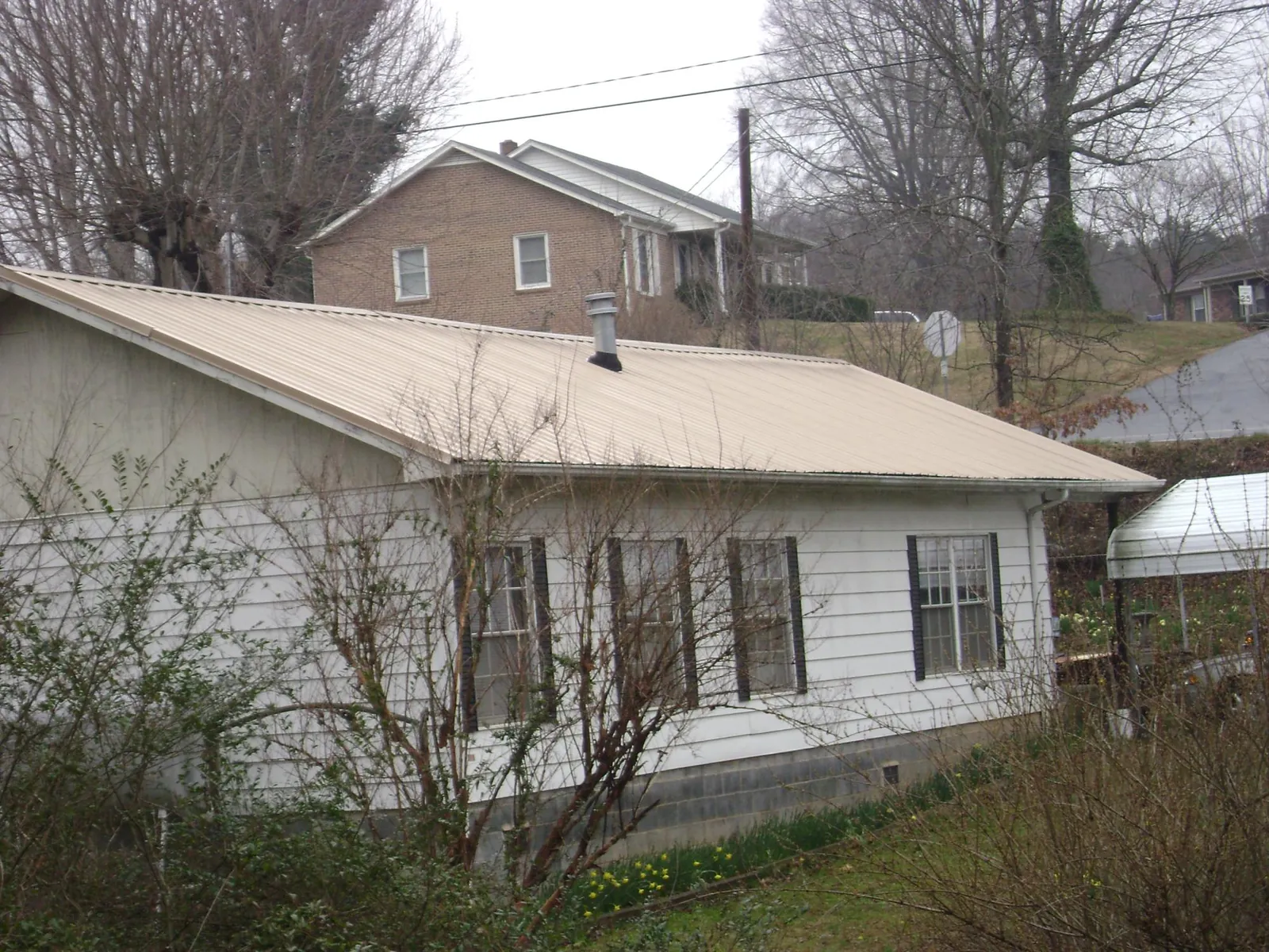 Tan metal roof on a white sided house set into a hillside — Commercial Roofing by Roofing Brothers in Furman