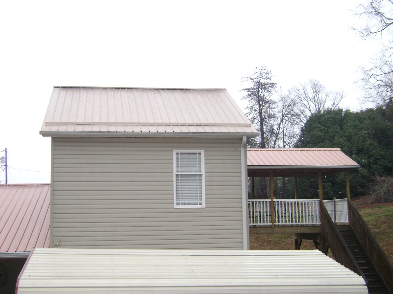 Tan metal roofs on a two story addition and attached porch, from a Roof Replacement job in Furman